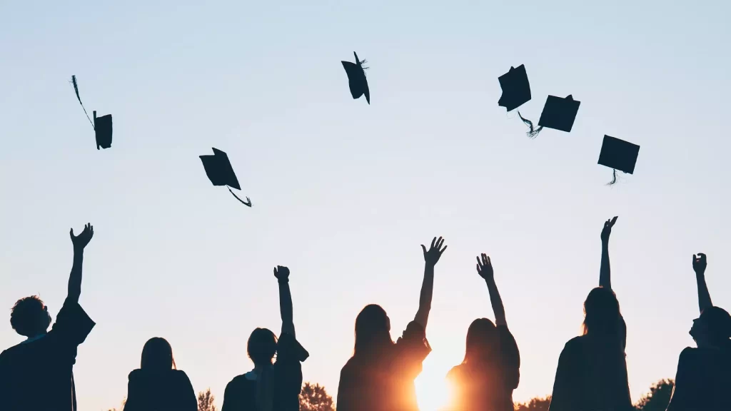 Gruppo di laureati che lanciano in aria i tocchi al tramonto, simbolo di gioia e celebrazione per la fine del percorso universitario – regali di laurea originali ed emozionanti per lui e per lei