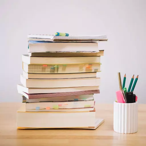Pila di libri e quaderni sulla scrivania di un laureato che vuole pubblicare la tesi